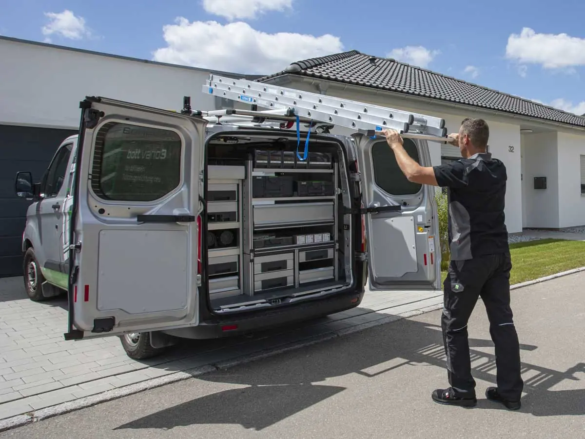 Techniker nimmt eine Leiter vom Dachträger mit Leiterlift eines Servicefahrzeugs mit bott vario3 Fahrzeugeinrichtung
