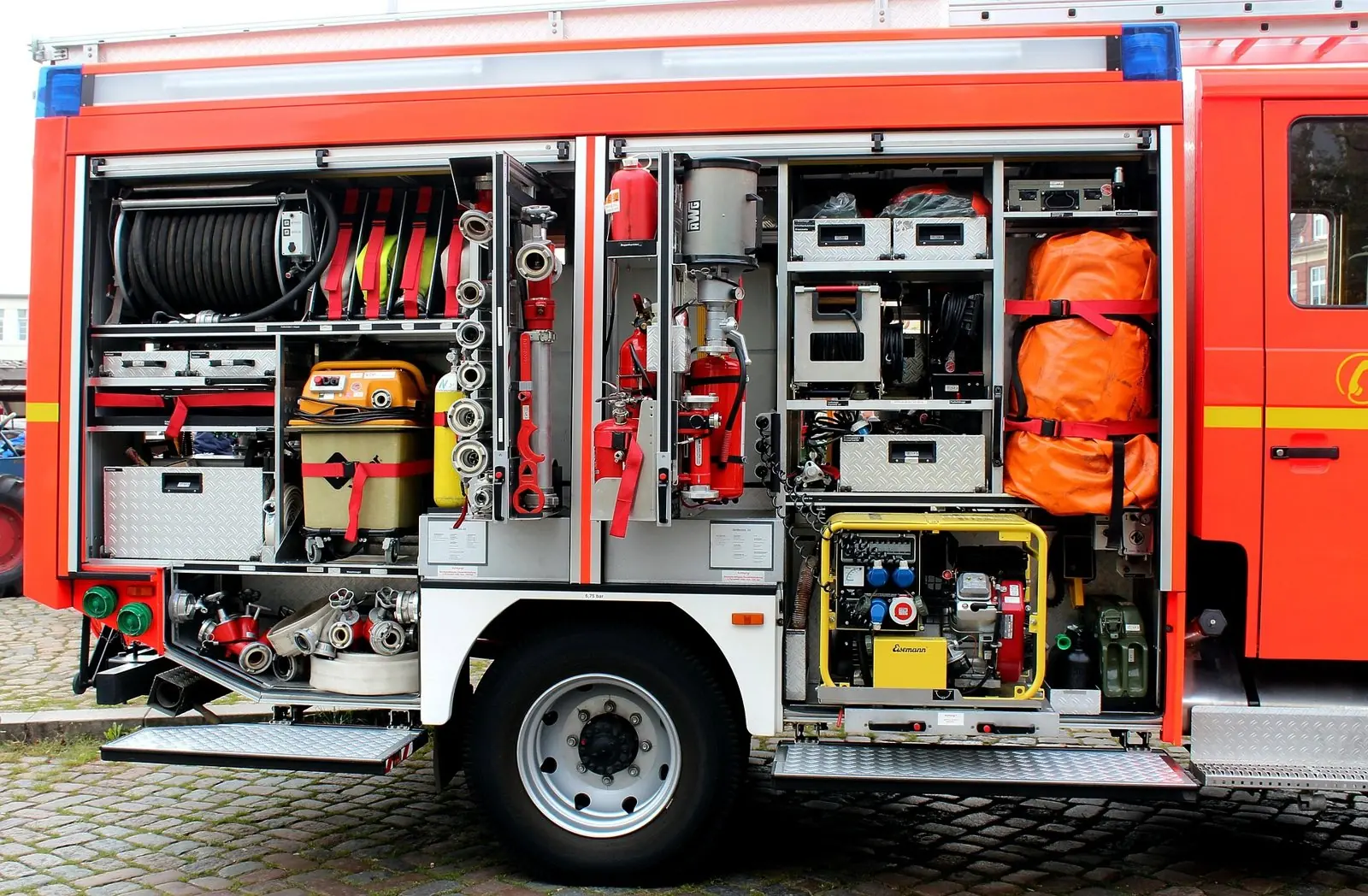 Geöffnete Geräteräume eines Löschfahrzeugs mit Schlauchhaspel, Feuerlöschern, Notstromerzeuger und Beladung